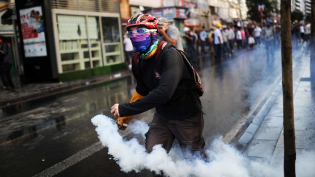 A protester throws back a tear gas canister at riot police during clashes in the streets near Taksim square.