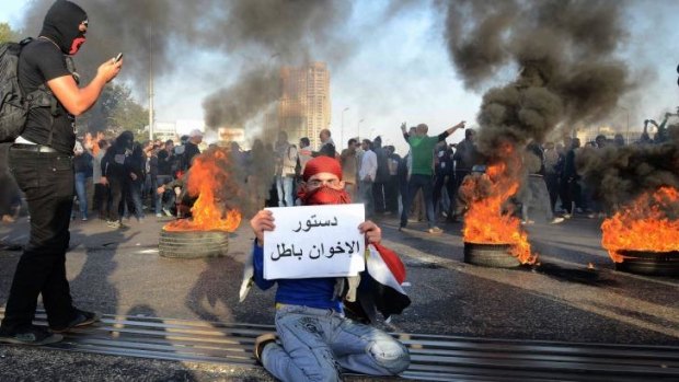An Egyptian protester holds a sign as other demonstrators, said to be members of Egypt's Black Bloc Anarchic group, burn tyres in Cairo.