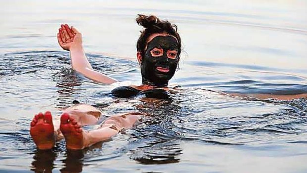 A tourist, her face covered with mud, floats near the Dead Sea resort of Kalia.
