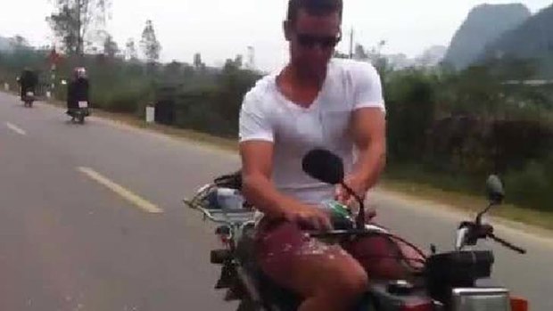 An Australian man prepares to skoll a beer while riding a motorbike without a helmet in Vietnam.