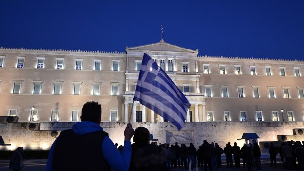 A man holds a Greek flag in front of the Greek parliament in Athens as people gather to support their government on Friday prior to the Eurogroup finance agreement.