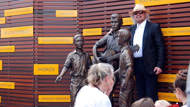 Barry Gibb poses with the statue of the young Bee Gees.