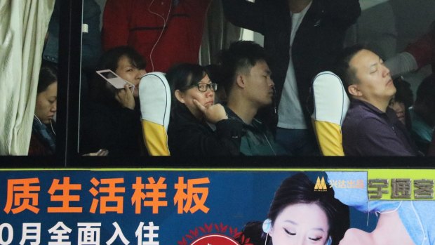 Commuters in Beijing during morning peak hour on board a bus emblazoned with property ads. 