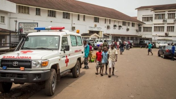 Before the lockdown ... boys, centre, walk past an ambulance, left, equipped to carry Ebola patients, outside the Connaught Hospital in Freetown, Sierra Leone. Shoppers have been stocking up for a stocking up for a three-day shutdown.