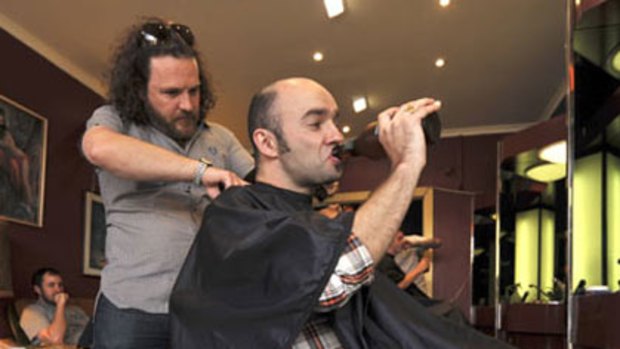 Joe Cowan sips on a cool beer as barber Craig Kershaw cuts his hair.