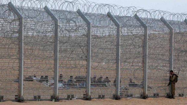Left out &#8230; the Eritrean asylum seekers sit and wait by the border fence as an Israeli soldier watches from the other side.