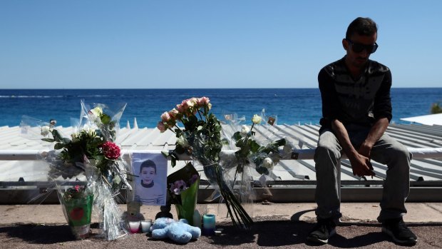 A man sits next to flowers and tributes set around a photograph of a small boy on the Promenade des Anglais in Nice on Saturday. 