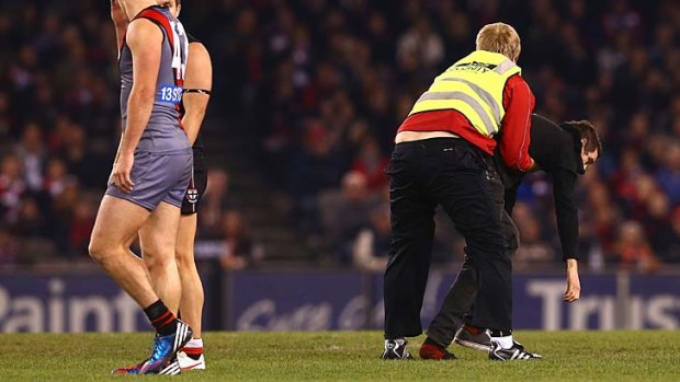 A pitch invader is tackled by security during the match between the Saints and the Bombers.