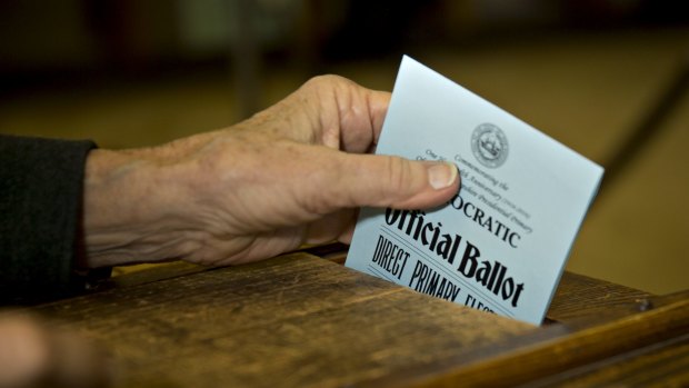 An election moderator places a Democratic ballot into a ballot box during New Hampshire presidential primary.