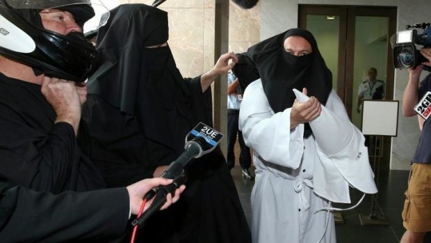 Protester Sergio Redegalli removes a Ku Klux Klan mask to reveal he is wearing a burqa underneath.