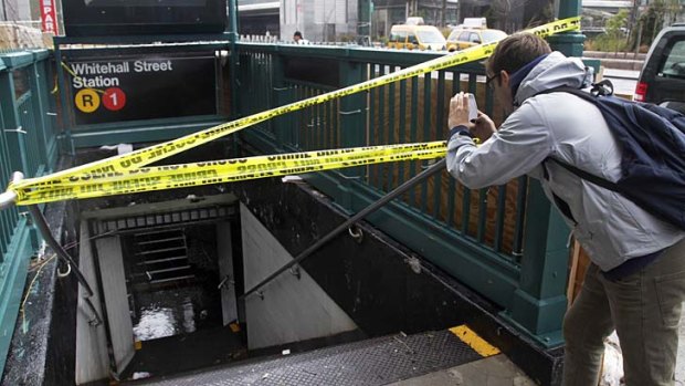 A man uses his smartphone to photograph a closed and flooded subway station in lower Manhattan.