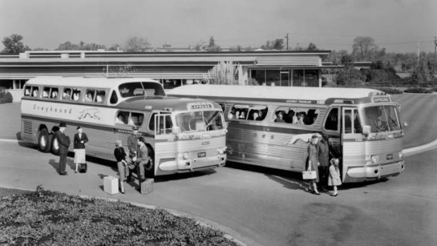 Two Greyhound Express coaches, with passengers waiting to board, at an American bus station in the 1960s.