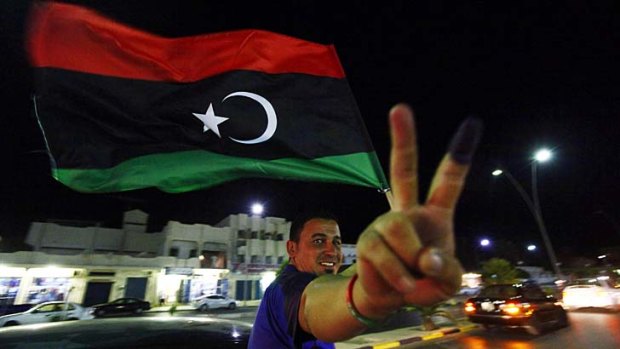 A man, with an inked finger, flashes the victory sign as he celebrates with the new Libyan flag at the end of voting day in Sirte July 7, 2012.