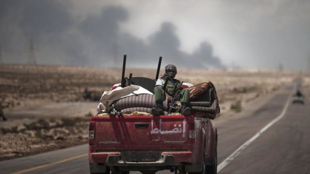 Black smoke rises from the Brega petrochemical facility as Libyan rebels drive on an armed pick-up truck towards the frontline.
