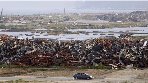 A car drives past a pile of wrecked vehicles, destroyed by the March 11th earthquake and tsunami.