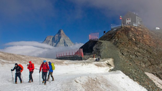 The Matterhorn rises above the clouds, a group of hikers and Rifugio Teodulo.