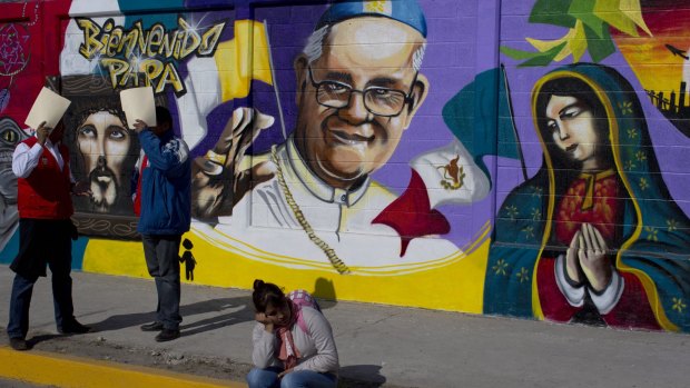 A woman sits in front of a mural of Pope Francis in Mexico City, a city the Pope is visiting this month.