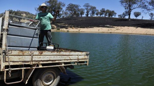 Jonathan Burgess fills up his water tank from the dam on his property near Yass on Wednesday after it was almost completely burnt out.