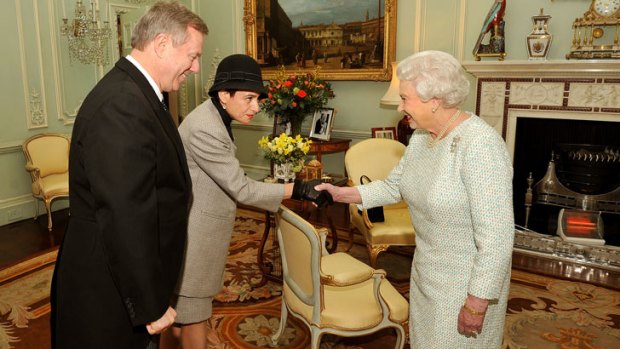 Queen Elizabeth II shakes hands with Sasha Rann as her husband High Commissioner of Australia Mr Mike Rann looks on in a room warmed by a two-bar electric fire.
