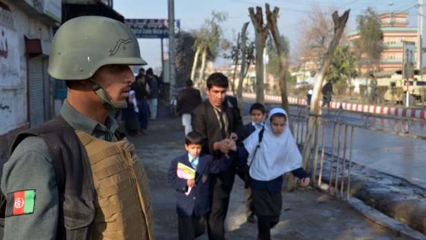 An Afghan member of the security forces stands guard as a man helps school children run from the site of clashes near Pakistan's consulate in Jalalabad, Afghanistan on Wednesday.