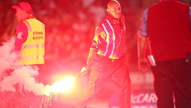 A security guard handles a flare during the A-League derby between Sydney FC and the Western Sydney Wanderers on Saturday.