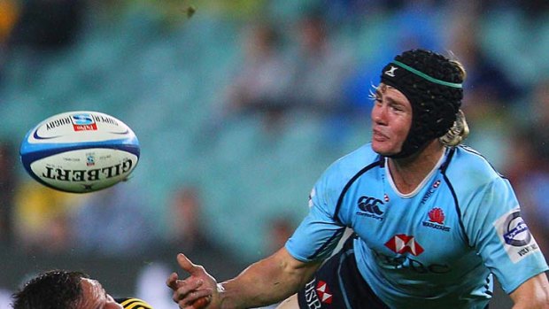 Berrick Barnes of the Waratahs passes as he is tackled.