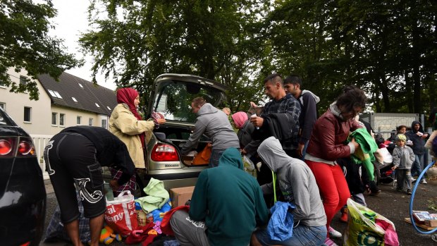 Refugees sift through donated clothing at the gates to the front entrance of a refugee camp near the town of Hilbersdorf, Germany in 2015.