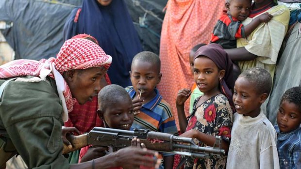 A government soldier on patrol in the streets of Somalia's war-torn capital demonstrates to Somali children how to use a Kalashnikov rifle.