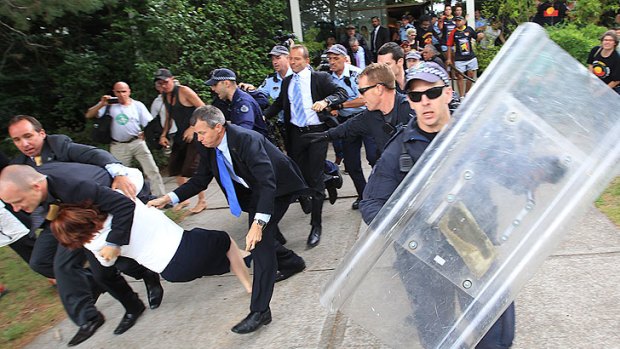 Julia Gillard is dragged away from the protest by her security officers.