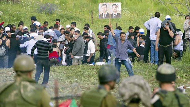 A demonstrator raises pictures of Syrian President Bashar al-Assad in front of Israeli soldiers after protesters crossed from Syria into the Israeli-annexed Golan Heights near the Druze town of Majdal Shams yesterday.