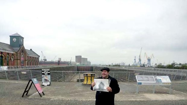 The dry dock at Harland and Wolff's shipyard in Belfast, where Titanic was fitted out before its fatal maiden voyage. The guide holding the old photograph shows the ship towering up out of the dry dock behind.