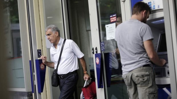A customer enters a Eurobank Ergasias SA bank branch as a man uses an automated teller machine outside shortly after opening in Athens.