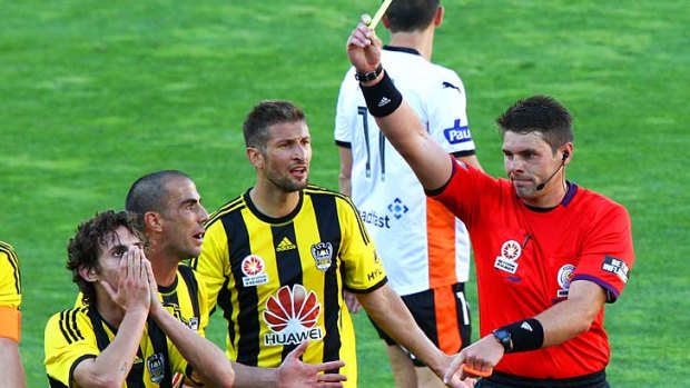 Referee Shaun Evans shows a yellow card to Albert Riera (left) of the Phoenix while teammates Manny Muscat and Vince Lia question the call.