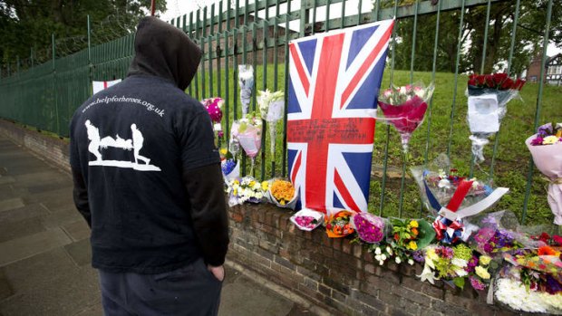 A man wearing a Help the Heroes T-shirt looks at floral tributes left at the scene where Drummer Lee Rigby was killed outside Woolwich Barracks in London.