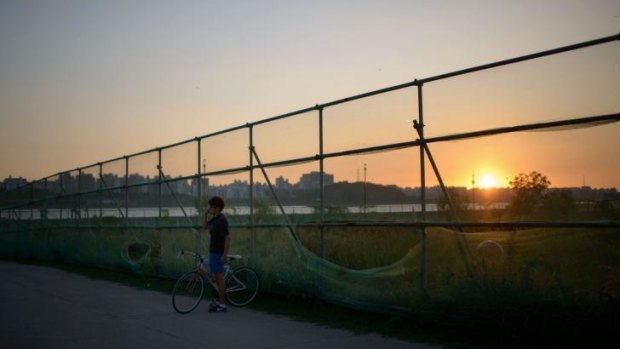 A cyclist talks on a mobile phone as the sun sets over the Han River, in which the American swimmer was arrested trying to swim to North Korea.