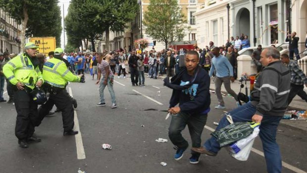 A man carrying a knife runs down a Notting Hill street in London while a man (background) struggles after being stabbed, as police and a bystander (right) react.