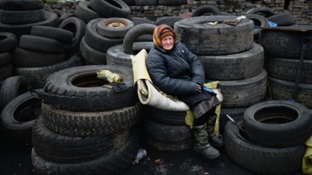 An elderly woman sits on tyres at a barricade in independence square.