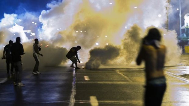 A protester reaches down to throw back a smoke canister as police clear a street after the curfew.