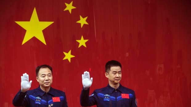 Chinese astronauts Jing Haipeng, left, and Chen Dong, right, wave from behind a glass enclosure during at the Jiuquan Satellite Launch Center in northwest China.