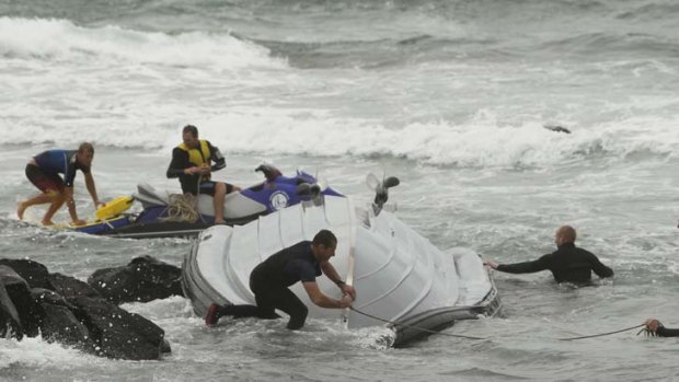 Tough even for the experts &#8230; officers struggle to pull a police rescue boat off rocks near Corrimal beach yesterday after it capsized in the rough surf.
