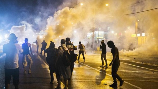 Protesters walk through smoke as police clear a street after the passing of the curfew last night.