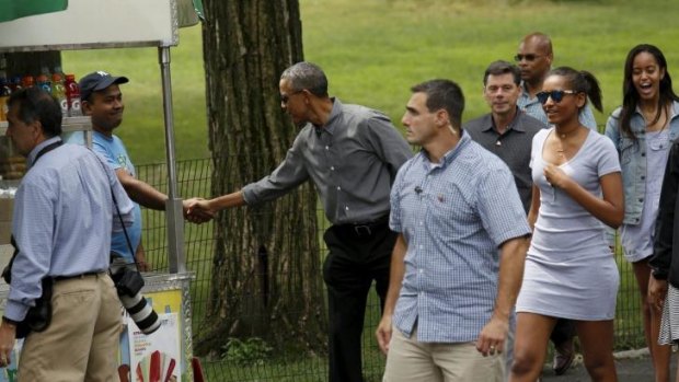 President Barack Obama shakes hands with a vendor while walking in Central Park with daughters Sasha and Malia.