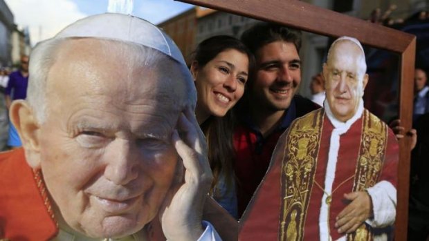 Two of the faithful pose with pictures of Pope John Paul II (L) and Pope John XXIII in front of St Peter's Square, in Rome ahead of their canonisation on Sunday.