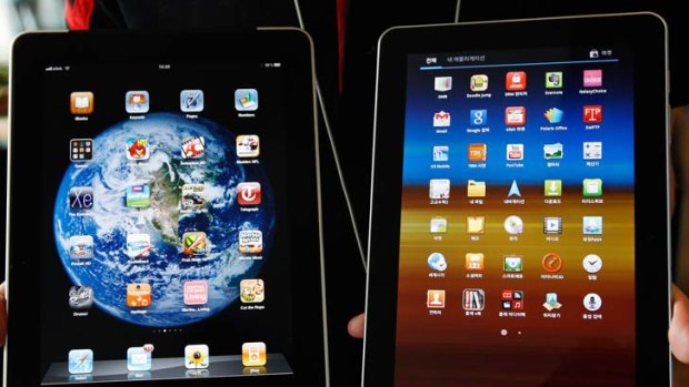 An employee of South Korean mobile carrier KT holds a Samsung Electronics' Galaxy Tab 10.1 tablet (R) and Apple Inc's iPad tablet as he poses for photos at a registration desk at KT's headquarters in Seoul August 10, 2011.