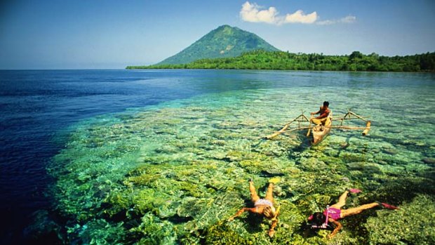A man in a traditional canoe watches two two snorkellers in Manado.