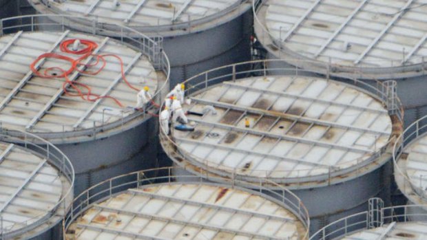 Workers stand on storage tanks at the Fukushima nuclear plant in Japan on Tuesday. A warning is being upgraded over toxic water emitting from the plant.