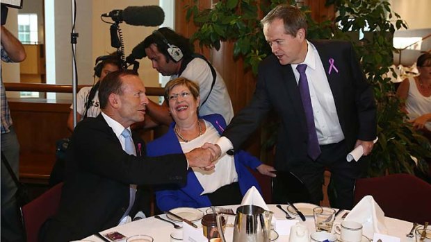 Prime Minister Tony Abbott, seated beside UN Women's Donelle Wheeler, greets Opposition Leader Bill Shorten during the International Women's Day parliamentary breakfast.