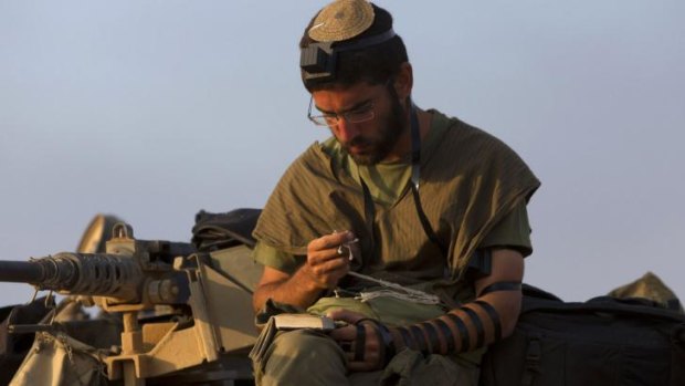 An Israeli soldier prays as he sits on a tank near the border with Gaza on Tuesday.