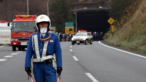 A policeman stands guard in front of emergency service vehicles on the road leading to the entrance of the collapsed tunnel.