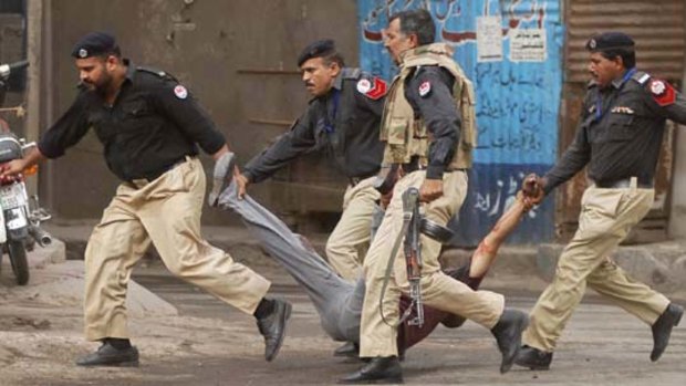 Policemen carry an injured worshipper away from the scene of a gun battle at a mosque in Lahore.